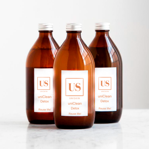 3 brown bottles of cleansers laid on top of a marble floor with the logo of uniSkin.